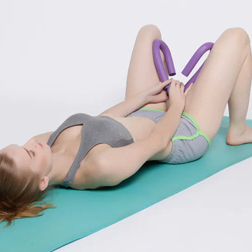 Woman exercising on a green mat with a purple portable thigh resistance trainer.