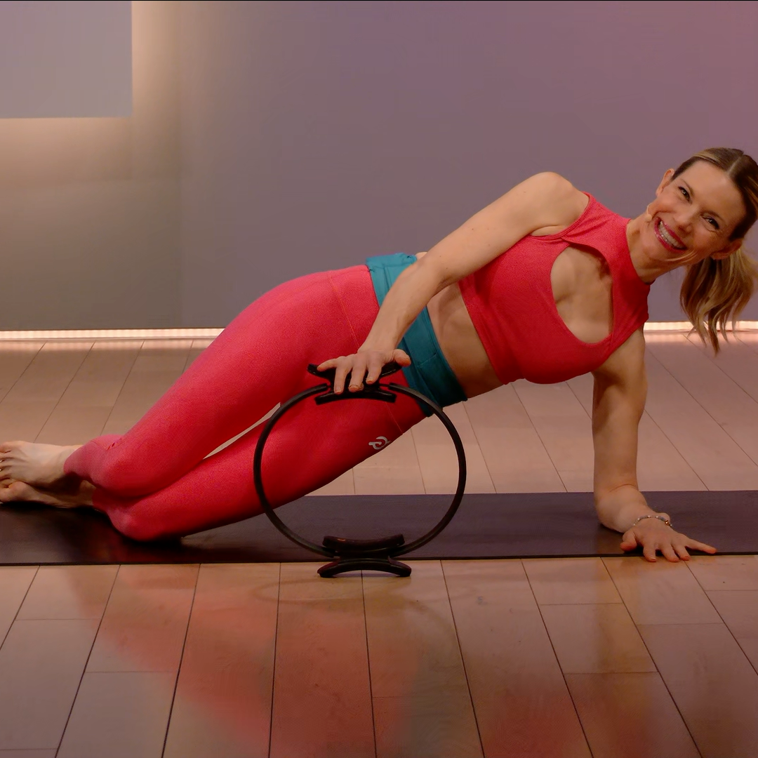 Woman in red tank top and leggings using a resistance ring on a mat.