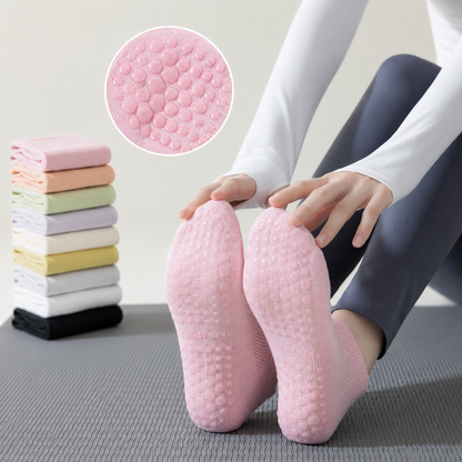 Woman wearing pink non-slip Pilates socks with silicone grip soles while sitting on a yoga mat indoors, showcasing breathable mesh fabric and traction for yoga and home workouts.